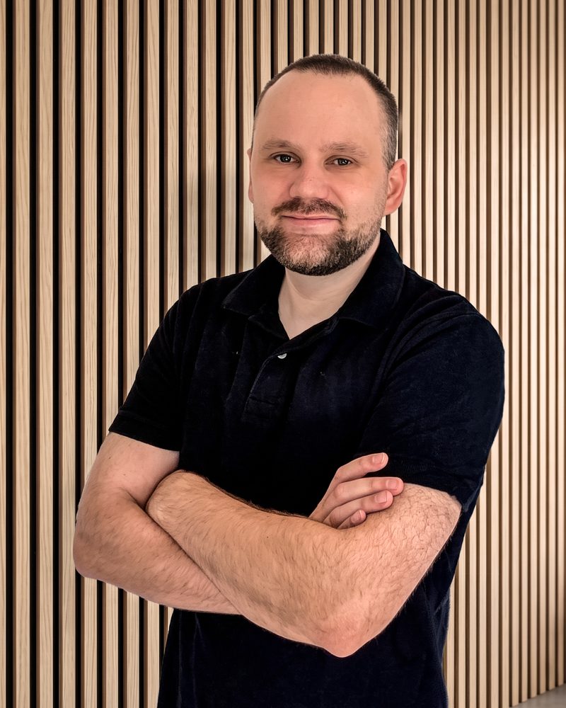 Iven Reese mit verschränkten Armen vor einer Holzlamellenwand